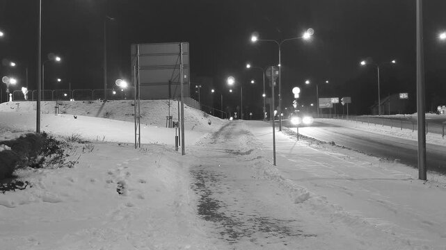 Zima w mieście nocą, zaśnieżone ulice w świetle podczerwonym. Spokojnie padający śnieg w zimową noc w mieście. Ulice miasta pokryte warstwą puszystego śniegu i oświetlone latarniami i światłami aut.