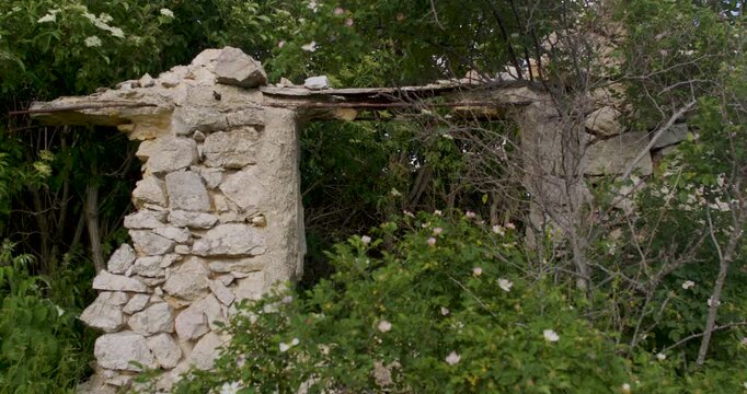 View of ruined stone doorway surrounded by dense plants and trees in rural Bosnia and Herzegovina. The abandoned architectural remains reflect historical rural life, decay, and natural reclamation ove