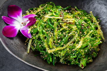 Fresh seaweed salad served in a bowl with a flower on the side. A bowl contains seaweed salad, garnished with sesame seeds and a purple flower on the edge. © white78