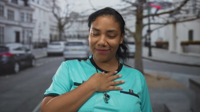 Woman referee wearing turquoise uniform smiling with hand on chest on street; pride trust dedication.