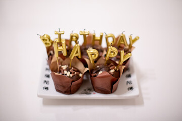 Chocolate cupcakes with golden birthday candles on white plate