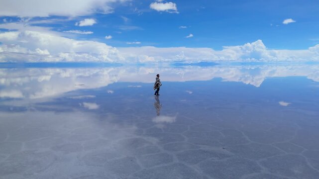 A solitary figure traverses the expansive Salar de Uyuni in Bolivia, captured under a clear midday sky 