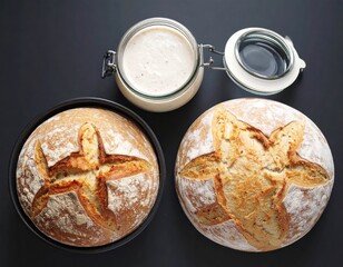Two Golden Brown Sourdough Breads One in a Dark Baking Pan Next to a Jar of Starter on a Black Surface