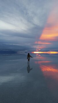 A solitary figure walks across the expansive Salar de Uyuni in Bolivia, capturing the surreal beauty of the salt flats during a stunning sunset