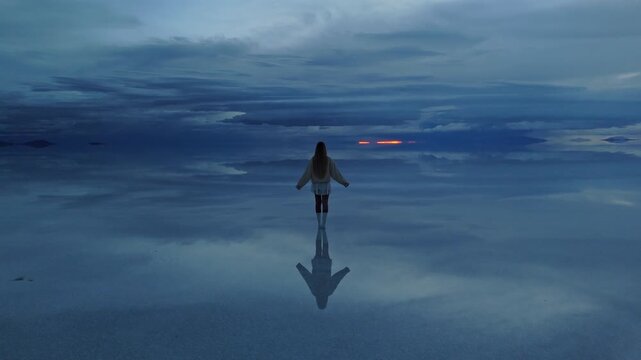 A solitary figure standing on the reflective surface of Bolivia's Salar de Uyuni during a tranquil late afternoon