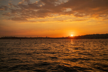 Naklejka premium Beautiful glowing sunset on the European side of Istanbul, Turkey from Bosphorus toward Karakoy and Eminonu, with the silhouettes of Galata Tower and Suleymaniye Mosque against burning sky