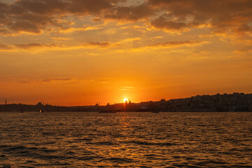 Naklejka premium Beautiful glowing sunset on the European side of Istanbul, Turkey from Bosphorus toward Karakoy and Eminonu, with the silhouettes of Galata Tower and Suleymaniye Mosque against burning sky
