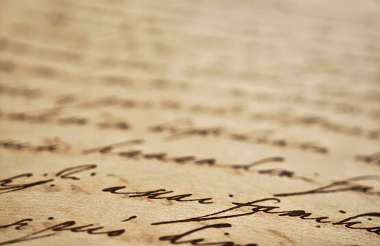 Extreme closeup of old handwritten manuscript on yellowed paper with cursive ink writing, shallow depth of field soft blurred background, vintage document texture history, literature, poetry, archival
