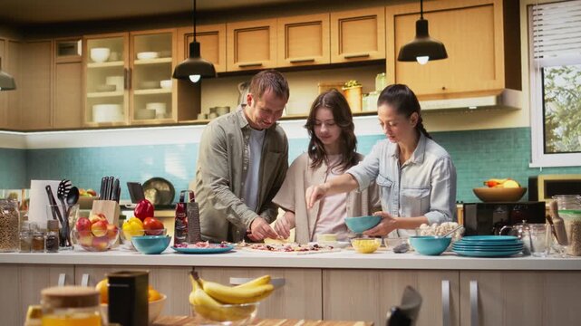 Family fun in the kitchen as everyone is layering cheese and mozzarella on the dough, preparing homemade pizza together. Warm scene captures joy and delicious homemade food. Camera A.