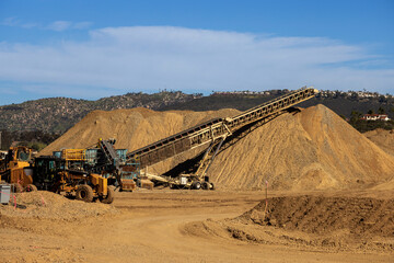 A conveyor machine and a large mound of dirt and gravel at a construction site