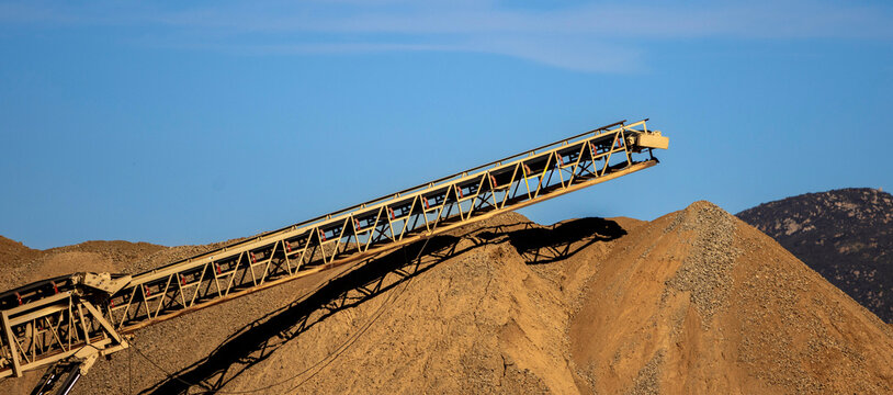 A conveyor machine and a large mound of dirt and gravel at a construction site