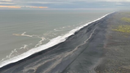 View of basalt stacks Reynisdrangar, black sand beach, church and city of Vik, Iceland