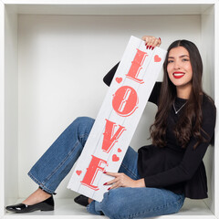 Young woman holding a sign with the word LOVE in a white cube setting
