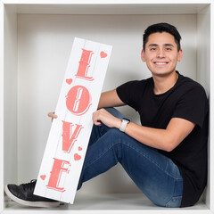 Young man holding a sign with the word love in a white cube, celebrating Valentine's Day