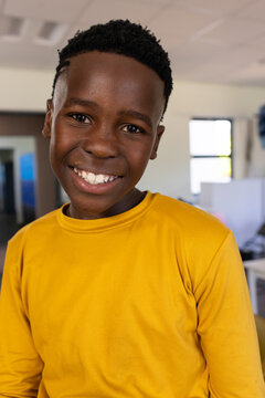 African male youth smiling, wearing yellow long-sleeve shirt at school with drop ceiling lights PC