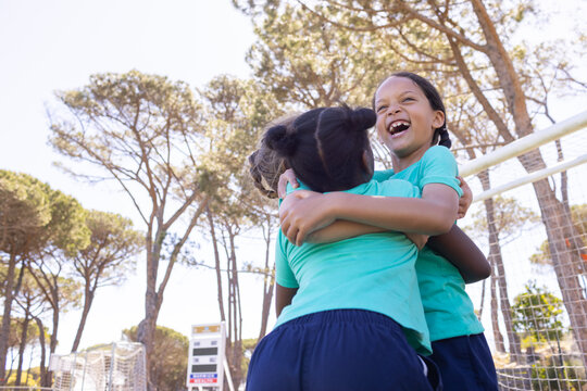 African American youth female soccer team hugging, celebrating on sunlit field near goal frame net