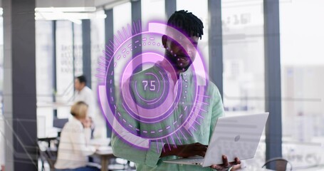 Holding open laptop, mature man wearing green shirt examining screen at open office, AR showing 75