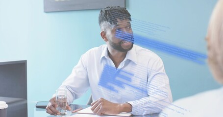 Speaking man in light-blue shirt holding clear glass, resting hand on notepad at small meeting room