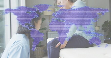 Kneeling blue-shirt woman checking green-shirt man on sofa touching knee at home, with map overlay