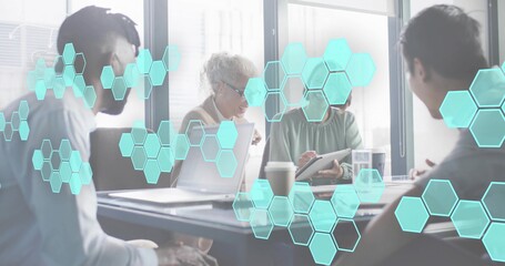 Talking office team in suits reviewing papers on laptops and tablet at meeting table, hex overlay