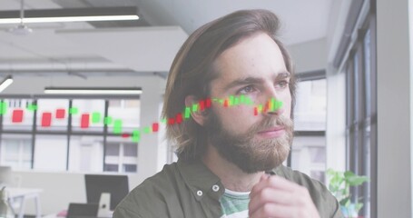Viewing candlestick overlay, bearded man in olive-green shirt studying data in open-plan office