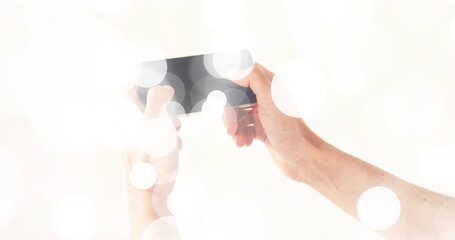 Showing bare arms and hands holding black smartphone at bright white backdrop, with bokeh overlays