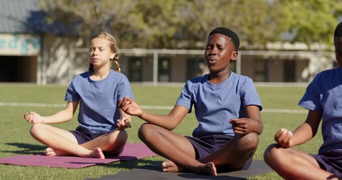 Diverse teen students at school following teacher cue, sitting on yoga mats in blue tees, chanting