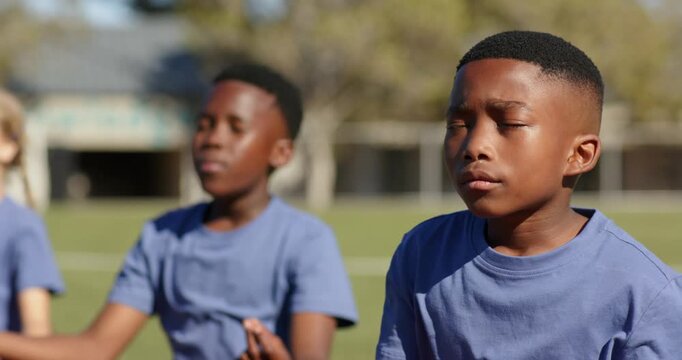 Teenage students responding to teacher cue, breathing and meditating on grass mat wearing blue tees