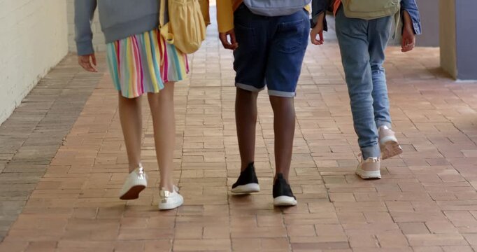 Diverse school-age children walking brick path backpacks on left child placing arm heading to exit