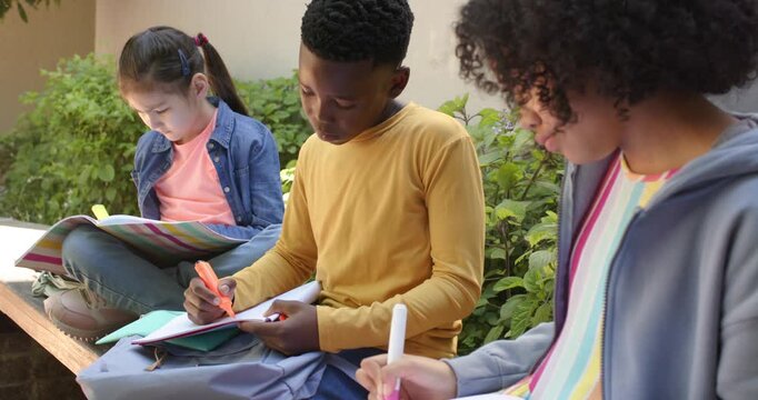 Diverse preteens sitting on bench using highlighters and flipping red folder while studying notes