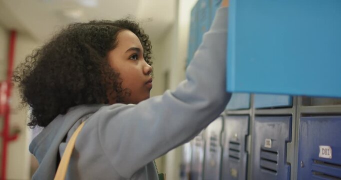 African American teen opening blue locker getting folder and moving yellow backpack strap for class