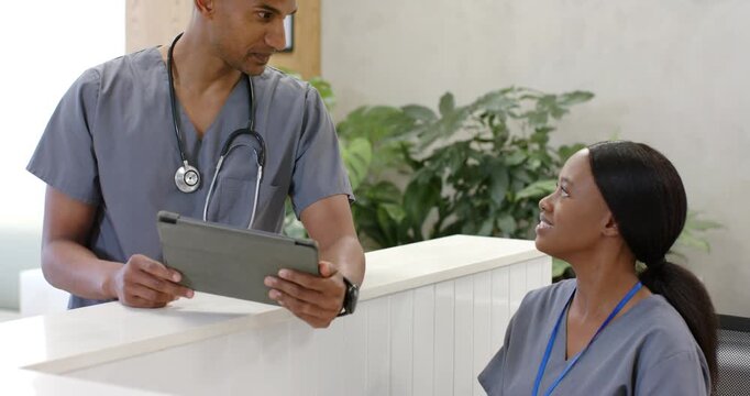 African American staff leaning on front desk, male clinician holding tablet, updating patient chart