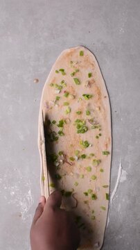 Overhead view of scallions on chinese pancake dough being made on grey countertop, process of making homemade scallion pancakes or cong you bing