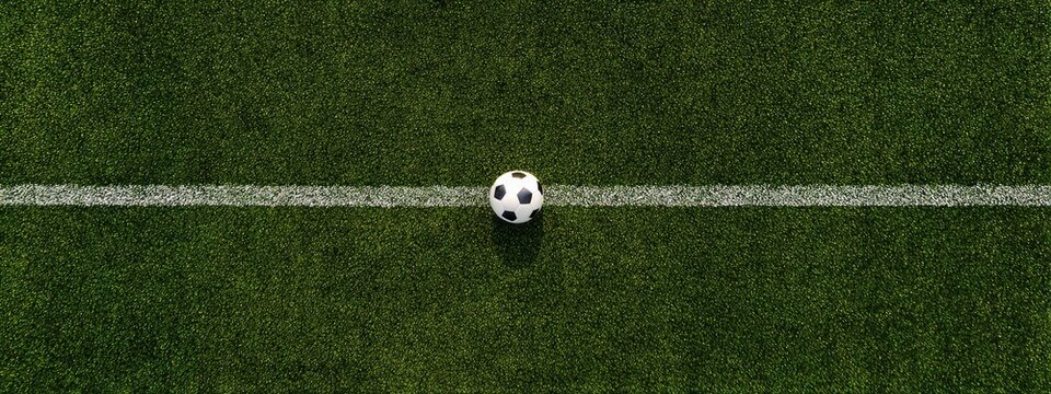 A top-down shot showcases a soccer ball resting on the center line of a grass field, the lines marking the playing area