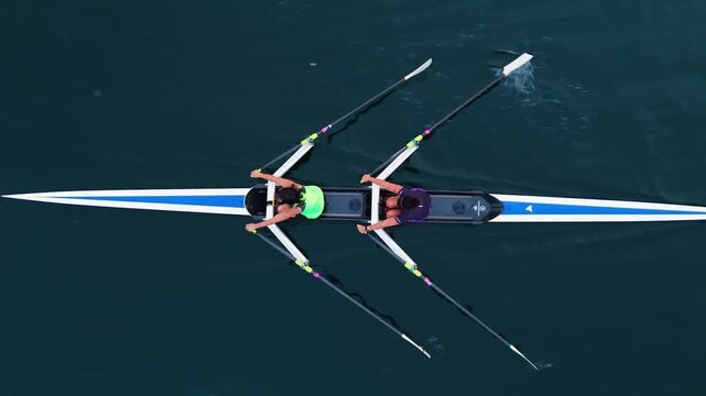 Top View Four young athletes row together in an eight-oar boat during sunrise training. Serene ocean and warm morning light frame focused preparation for rowing competition.