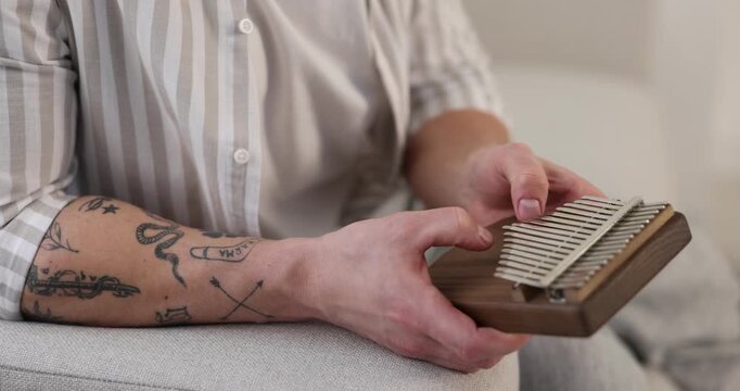 Man playing kalimba on sofa at home, closeup. Camera moving right