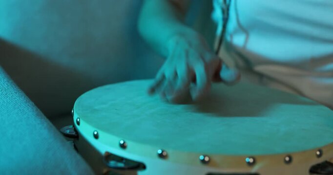 Woman playing tambourine in color light at home, closeup