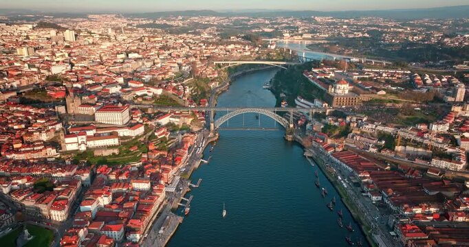 Aerial view sunset panorama of Porto city spreads along Douro River with red roof buildings, historic Ribeira waterfront and iconic Luis I Bridge linking Porto and Vila Nova de Gaia under bright sun