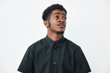 Obraz premium Young black man with dark skin wearing black shirt looking up thoughtfully on white background. Portrait of African ethnicity male with short curly hair and casual style.