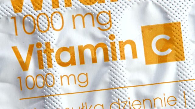 Extreme macro shot of vitamin C 1000 mg blister pack foil with orange label text on white dimpled packaging, pharmacy over the counter supplement dosage, readable print, full frame, simple concept