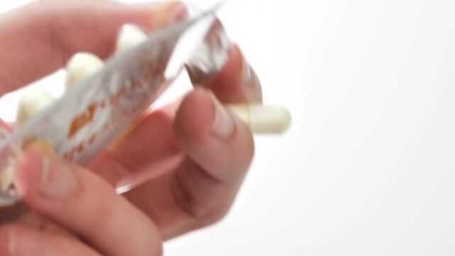 Close up macro of hand pushing vitamin capsule out of blister pack on white background, removing pill from foil packaging in studio shot, closeup healthcare medication supplement concept, copy space