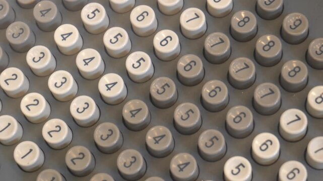 Closeup panning footage of vintage mechanical adding machine numeric keypad with round white and gray number buttons, worn retro office calculator keys forming full frame texture background, no people