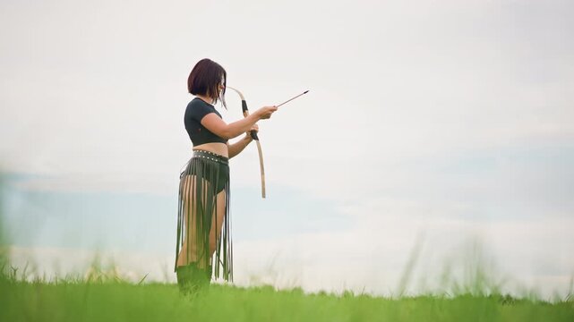 woman archer standing in grassland, wearing leather skirt, drawing wooden bow with steady aim toward distant horizon, soft overcast sky, tall green grass foreground, cinematic solitary mood conveying
