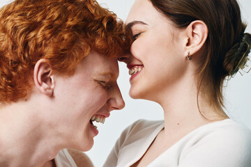 Naklejka premium Young couple with close faces laughing and enjoying tender moment, smiling woman and man with red hair in casual clothes on white background expressing happiness and love.