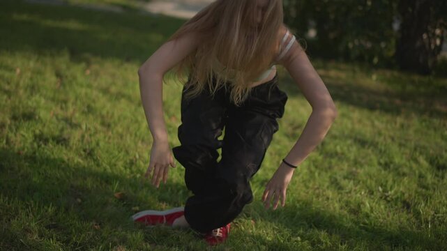 young white woman practicing street dance in sunlit park grass, long hair covering face, moving from seated floorwork to powerful standing strikes and expressive arm lines, raw energy, rehearsal vibe,