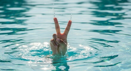 A hand emerges from crystal clear blue water, forming a peace sign with fingers and droplets