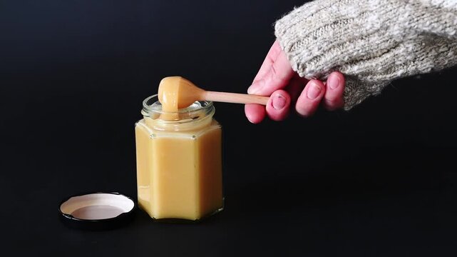 Person using Honey Dipper to Drop a Dollop of Creamed Honey into the jar, black background