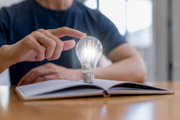 Man touching glowing light bulb above open book, creativity and idea concept. Innovation, learning inspiration, knowledge growth, problem solving, education and modern technology thinking.