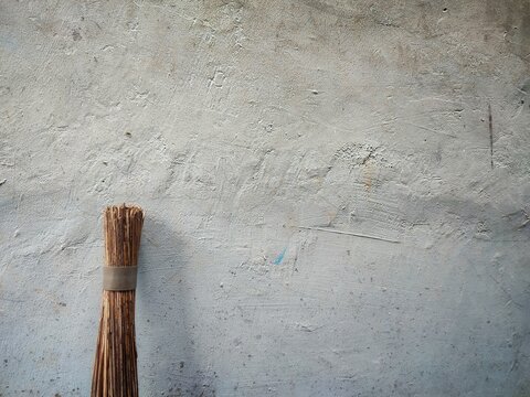 traditional wooden broom leaning against a rough weathered gray concrete wall