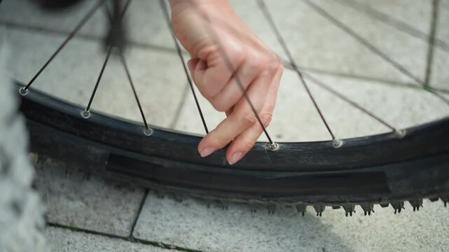 closeup bicycle tire hand removing thorn from sidewall delicate female hand pulls embedded thorn from wheel spoke area on city pavement textured tread and valve visible mood of quiet perseverance